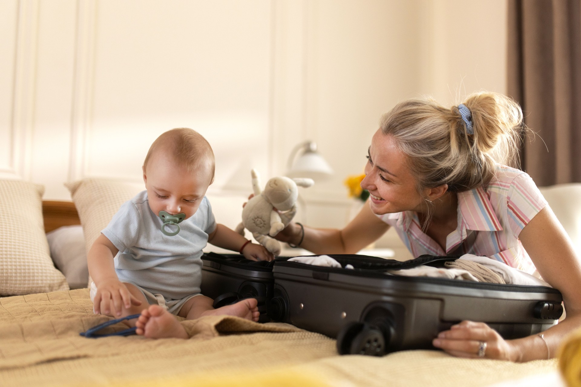 young mom prepring for a family trip , packing a suitcase in a cozy bedroom while her baby sits