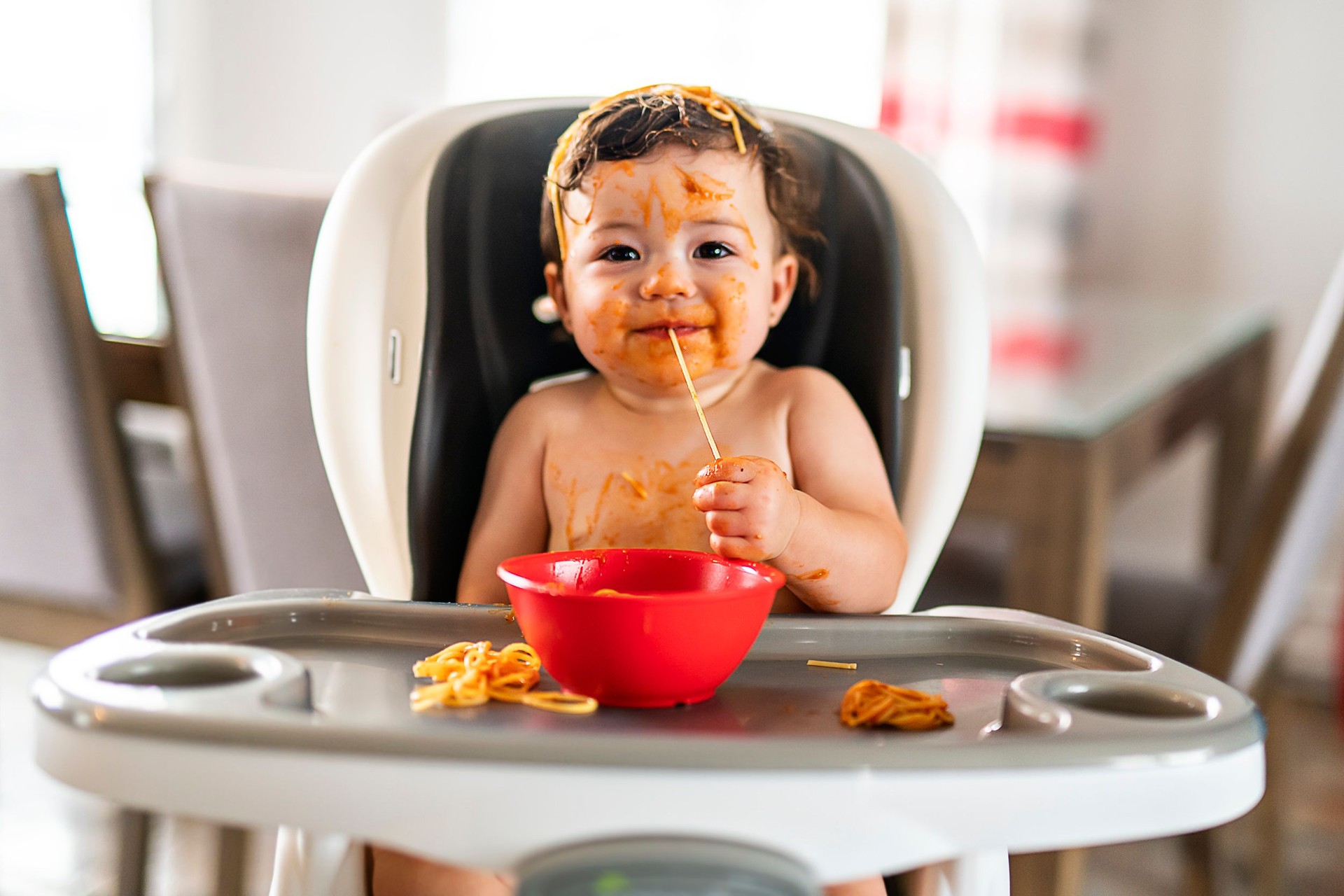 child girl, eating spaghetti for lunch and making a mess at home in kitchen